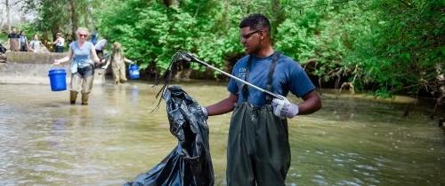 A student stands in a river doing trash clean up